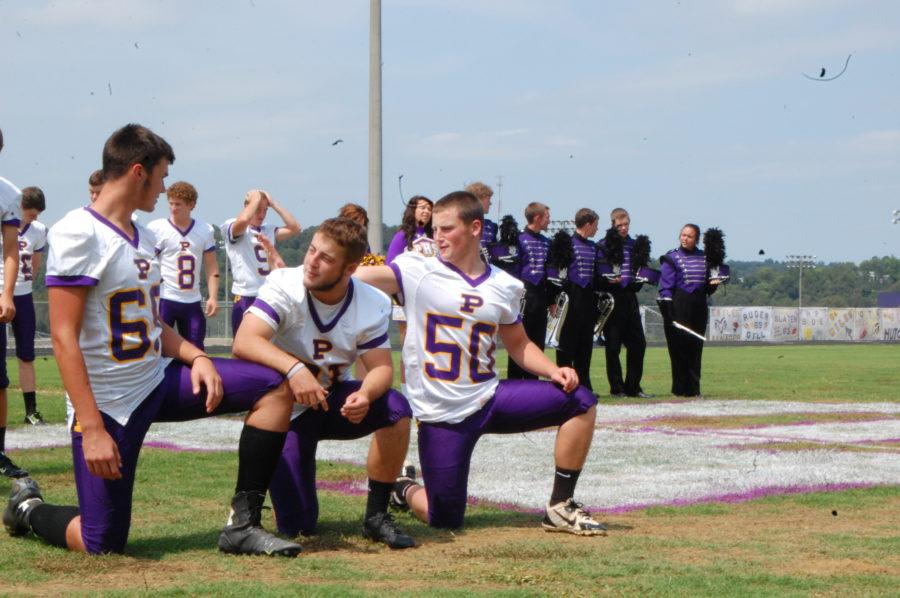 The football boys take a knee and wait for the photographer to snap a picture.