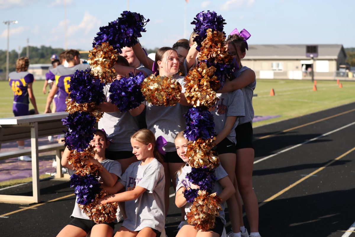 Junior high cheer team makes a "H" with their pom-poms.