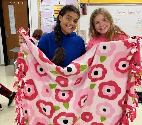 Sophomore Cheyenne Hopper and freshman Sofia Smith pose with a blanket they made as part of Tri-Hi-Y.