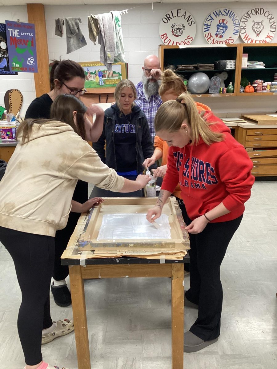 Junior Emilee Burton and seniors Madi Collier, Maddie Vernon, Ava Hall, and Abby Poe print one of the posters, while art teacher Chris Jones supervises.